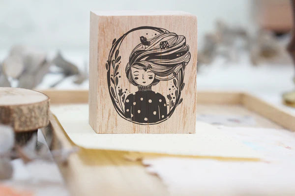 Wooden stamp with a design of a girl encircled in a wreath portrait with long hair and a bird